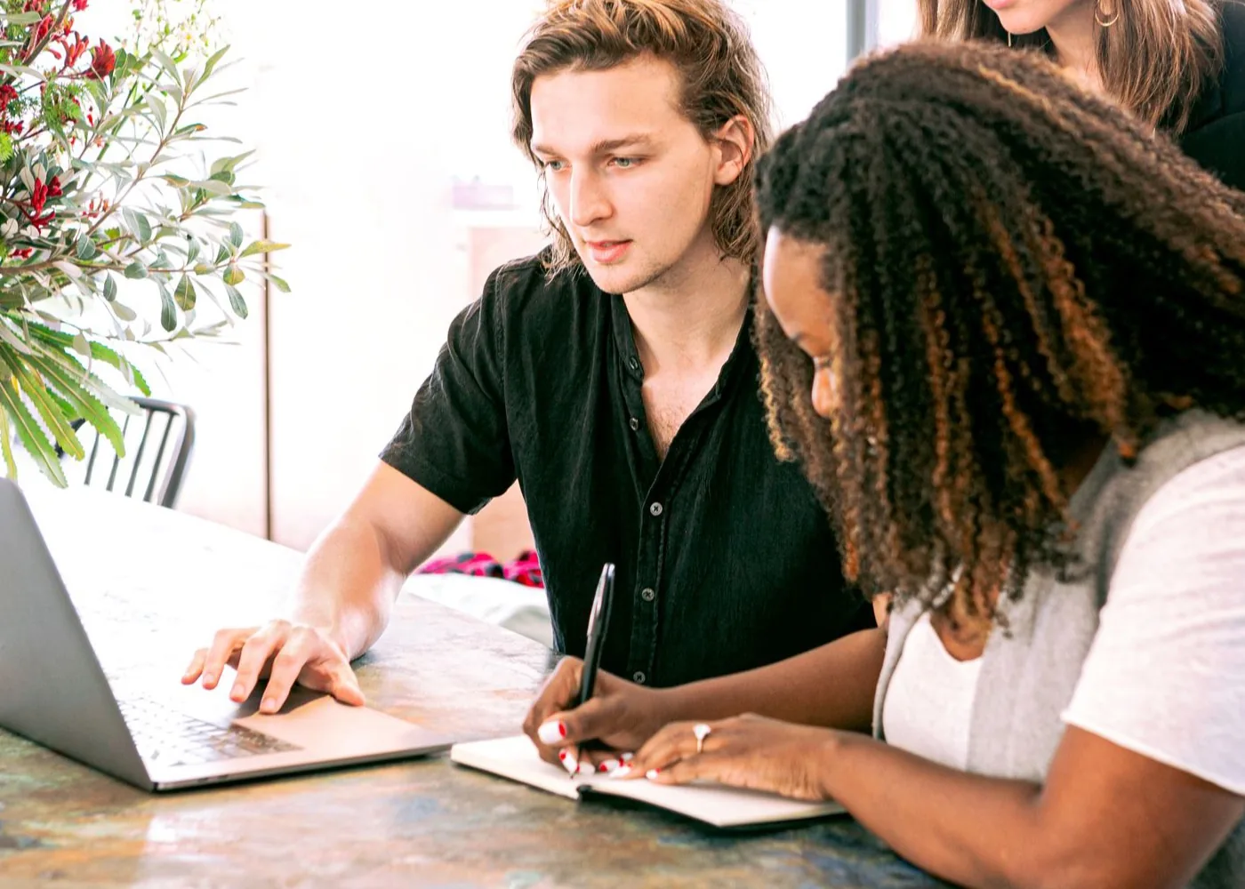 People reviewing a laptop and taking notes together in a sunlit workspace